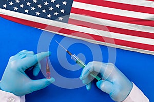 Hands of doctor holding syringe and coronavirus COVID-19 vial vaccine on flag USA