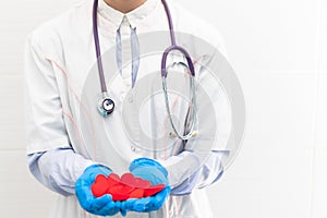 The hands of a doctor in a white medical coat and rubber gloves with a phonendoscope hold a lot of red hearts in the hospital.
