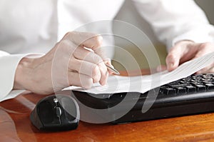 Hands with document and pen on a computer keyboard