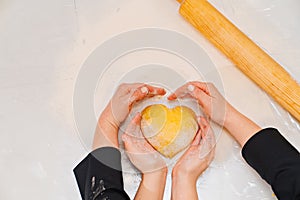 hands with dough in the shape of a heart, flour and eggs on the table.