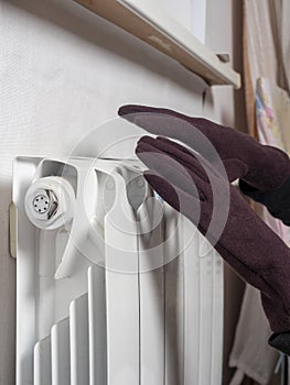 Hands dressed in brown gloves are attached to a white central heating battery. The concept of heating devices. winter season. Side