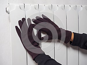 Hands dressed in brown gloves are attached to a white central heating battery. The concept of heating devices. winter season. Side