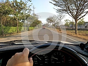 Hands driving a car on on steering wheel of a car and empty asphalt road