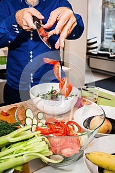 Hands drop chopped tomatoes into a bowl of vegetables