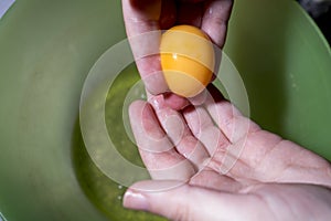 Hands with an egg yolk in the background a yellow bowl. photo