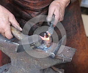 Hands of an elderly blacksmith working iron with a hammer and th