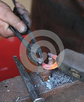 Hands of an elderly blacksmith working iron with a hammer and th