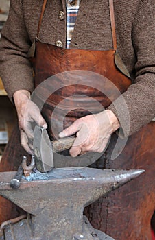 Hands of an elderly blacksmith working iron with a hammer and th
