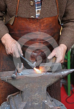 Hands of an elderly blacksmith working iron with a hammer and th