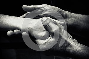 Hands of an elderly man holding the hand of a younger man.