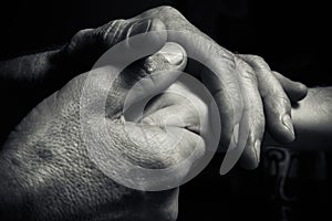 Hands of an elderly man holding the hand of a younger man.