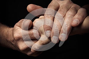 Hands of an elderly man holding the hand of a younger man.