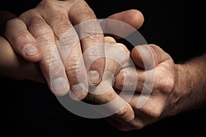 Hands of an elderly man holding the hand of a younger man.