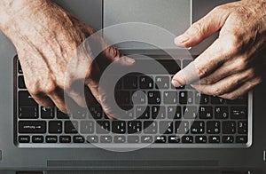 Hands of an elderly man learning to use computer, typing on a laptop, top view