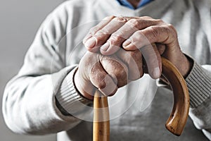 Hands of an elderly man resting on a walking cane
