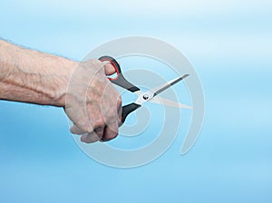In the hands of an elderly man, scissors cutting something. An old man demonstrates how to cut with scissors on a blue background
