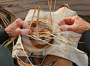 hands of an elderly man weave a wicker