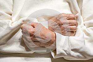 Hands of elderly woman clenched in fists on her chest