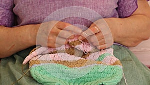 Hands of an elderly woman close-up knits on knitting needles from colored yarn