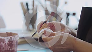 Hands of an elderly woman painting a little clay cup with dusty pink color