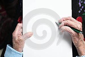 Hands of an elderly woman with a sheet for writing text. Drawing up a will.
