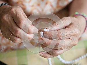 Hands of elderly woman threading a necklace