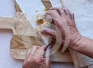 Hands of an elderly woman wrap meat rolls on the background of a cutting Board