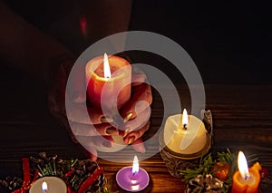 The hands of an elderly woman wrapped around a burning bright candle