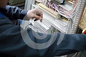 Hands of electrician assembling industrial HVAC control cabinet in workshop. Close-up photo.