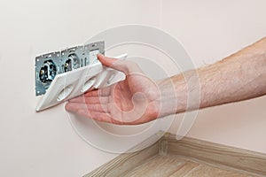 The hands of an electrician installing a wall power socket.