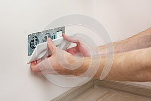 The hands of an electrician installing a wall power socket.