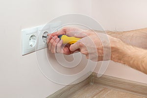 The hands of an electrician installing a wall power socket.