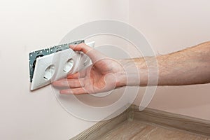 The hands of an electrician installing a wall power socket.