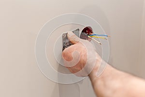 The hands of an electrician installing a wall power socket.