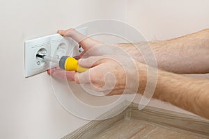 The hands of an electrician installing a wall power socket with screwdriver.
