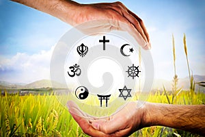 Hands encompassing symbols of various religions with nature background