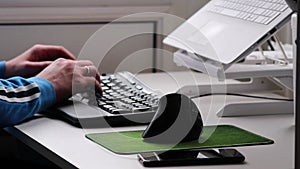 Hands of European man working at home in home office with ergonomic keyboard and ergonomic mouse white notebook black smartphone