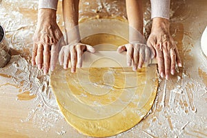 Hands of european small girl and elderly grandmother make dough with rolling pin for pizza and cookies