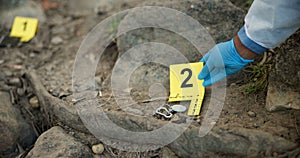 Hands, evidence marker and csi for investigation at crime scene with keys in ground or hazmat for safety in forest