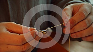 The hands of an experienced tailor thread a tailor`s needle to make a bag made of genuine leather.