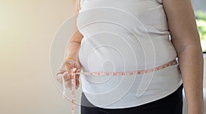 Hands of fat overweight woman measuring her waist size with a measuring tape