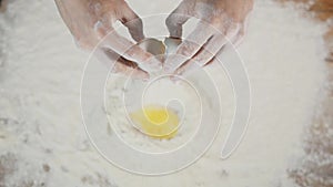 Hands of a female bakery chef breaking an egg into a heap of measured flour while making bread with a bunch of wheat