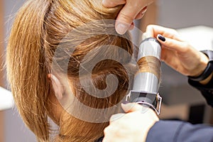 Hands of female hairstylist curls hair client with a curling iron in a hairdressing salon, close up.