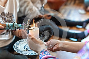 Hands of a female shaman with a candle lighting a bundle of cinnamon in a healing ceremony