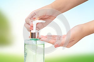 Hands female using wash hand sanitizer gel pump dispenser blurry green nature background