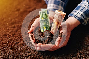 Hands with fertile soil and euro money banknotes