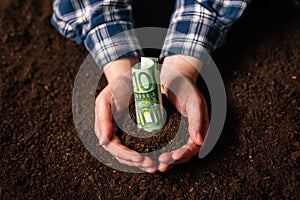 Hands with fertile soil and euro money banknotes