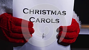 Hands in festive gloves holding Christmas carols music song sheet