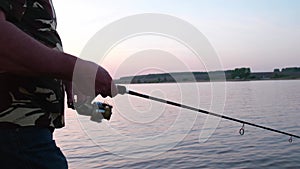 Hands of a fisherman close-up, a man holding a fishing rod, spinning the reel.