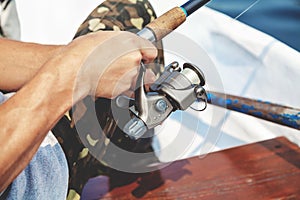 Hands fisherman holding fishing rod and reel handle is rotated
